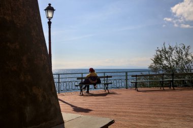 Baharın erken saatlerinde güneşli bir günde bir bankta oturan kadın.