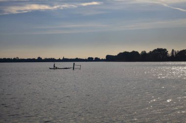 Alacakaranlıkta gölde sandalda kürek çeken bir adam.