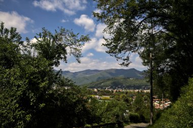 Güneşli bir günde, arka planda bir dağ sırtı ve bir kasaba olan bir ormanda Paved Yolu