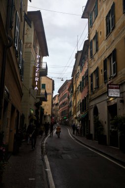 Hafif bir yağış sırasında Cenova Nervi 'de yüksek binaları ve dükkanları olan yokuş yukarı bir yol