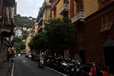 Hafif bir yağış sırasında Cenova Nervi 'de yüksek binaları ve dükkanları olan yokuş yukarı bir yol