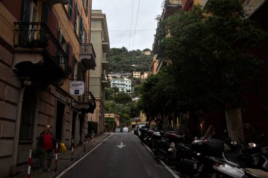 Hafif bir yağış sırasında Cenova Nervi 'de yüksek binaları ve dükkanları olan yokuş yukarı bir yol