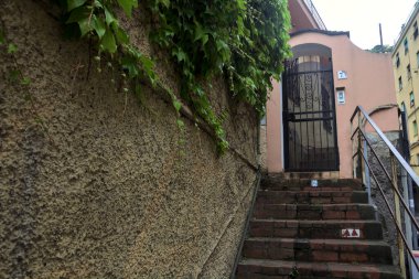 Bulutlu bir günde, bir duvarın yanında merdiven ve dar bir sokak ve bir bina.