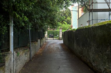 Beton duvarlar ve ağaçlarla çevrili bir yan yol.