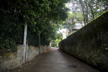 Beton duvarlar ve ağaçlarla çevrili bir yan yol.