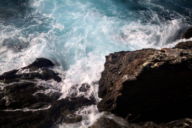 Güneşli bir günde dalgalar kayalıklara çarpıyor.