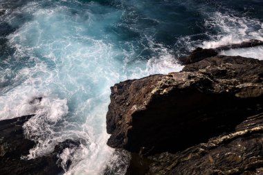 Güneşli bir günde dalgalar kayalıklara çarpıyor.
