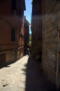 Güneşli bir günde, yüksek bir binayla taş bir köprü arasındaki sokakta.