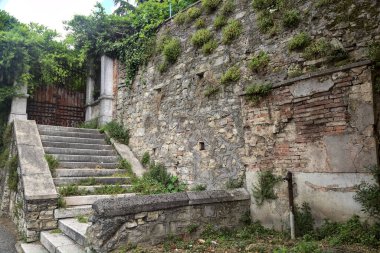 Bulutlu bir günde taş bir duvarın yanındaki paslı kapıya çıkan aşınmış taş merdiven.