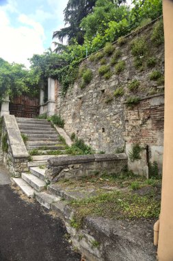 Bulutlu bir günde taş bir duvarın yanındaki paslı kapıya çıkan aşınmış taş merdiven.