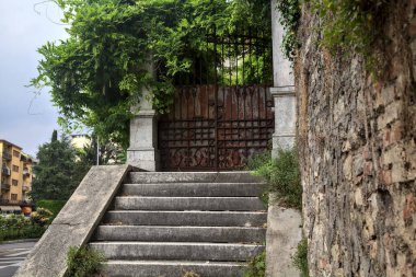 Bulutlu bir günde taş bir duvarın yanındaki paslı kapıya çıkan aşınmış taş merdiven.