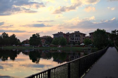 Gün batımında ağaçlarla çevrili bir gölde köprü.