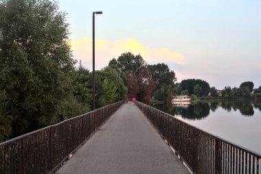 Gün batımında ağaçlarla çevrili bir gölde köprü.