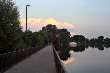 Gün batımında ağaçlarla çevrili bir gölde köprü.