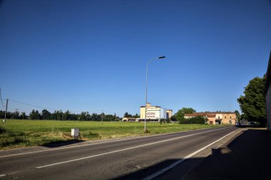 Güneşli bir günde bir depo ve köşkü olan kırsal bölgede yol.