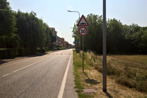 Road next to a field and a row of houses in the countryside on a sunny day