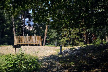 Parktaki küçük açık bir alanda ahşap bir çite yaslanan bank.