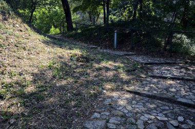 Güneşli bir günde, parkın korkuluğunda, gölgede, kaldırımlı bir yolda eğildim.