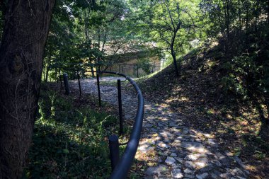 Güneşli bir günde, parkın korkuluğunda, gölgede, kaldırımlı bir yolda eğildim.