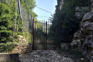 Rusty gate and fence at the entrance of an abandoned trail by the side of a cliff in the shade