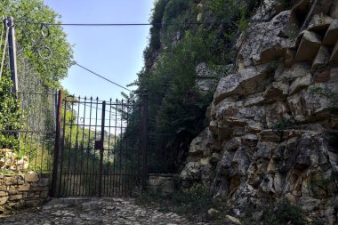 Paslı kapı ve çitler, terk edilmiş bir patikanın girişinde, gölgede bir uçurumun kenarında.