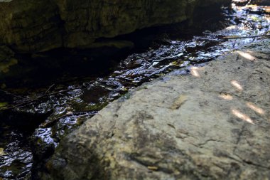 Gölgedeki kayaların arasından akan su yakından görülüyor.