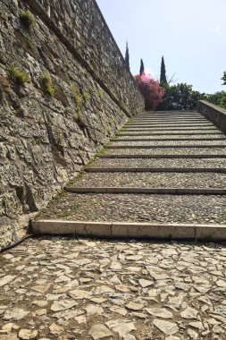 Güneşli bir günde, bir şatoda taş bir duvarın yanında kaldırımlı bir geçit ve adımlar.