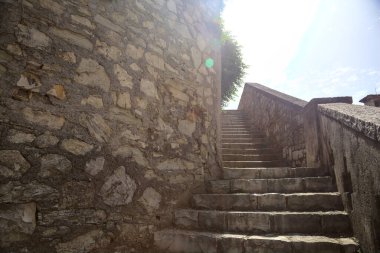 Staircase with balustrade next to a stone wall counter lit by the sun