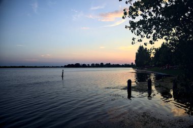 Yazın bir gölün üzerinde gün batımı kıyıların siluetiyle