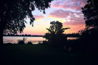 Yazın bir gölün üzerinde gün batımı kıyıların siluetiyle