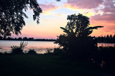 Yazın bir gölün üzerinde gün batımı kıyıların siluetiyle