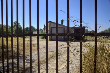 Abandoned warehouse behind a closed gate on a sunny day in the countryside