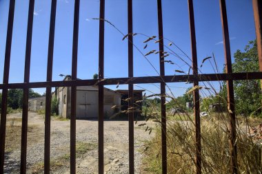 Abandoned warehouse behind a closed gate on a sunny day in the countryside