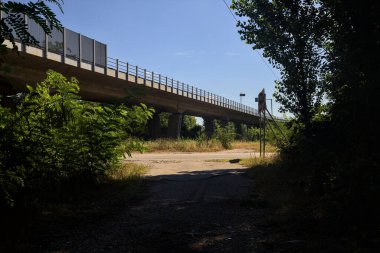 Crossing between a dirt road in the shade and a main road next to a highway on a summer day in the italian countryside
