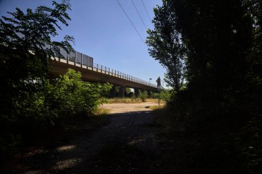 Crossing between a dirt road in the shade and a main road next to a highway on a summer day in the italian countryside