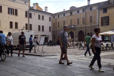 Square with restaurant tables and people passing by on a cloudy day