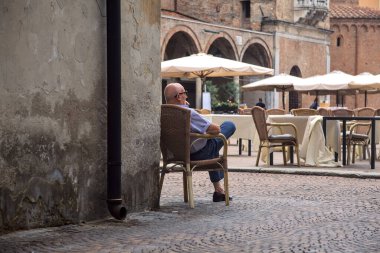 Old man sitting on a chair by the corner of a building