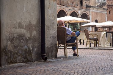 Old man sitting on a chair by the corner of a building
