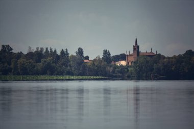 Güneşli bir günde, küçük bir köyü ve uzak bir koruluğu olan bir gölün kıyısında.