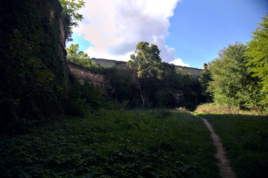 Güneşli bir günde, tahkimat duvarı ile orman ağaçları arasındaki açık bir alanda yol.