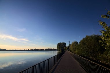 Gün batımında bir gölün üzerindeki köprüdeki patika.