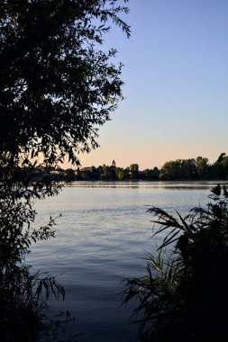 Gün batımında göl ağaçlarla çevrili ve kıyıdan görülüyor.