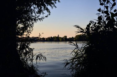 Gün batımında göl ağaçlarla çevrili ve kıyıdan görülüyor.