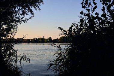 Gün batımında göl ağaçlarla çevrili ve kıyıdan görülüyor.