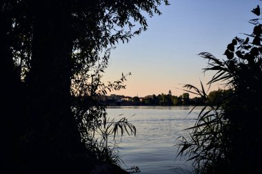 Gün batımında göl ağaçlarla çevrili ve kıyıdan görülüyor.