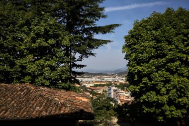 Gökyüzünden görünen şehir, güneşli bir günde ağaçlar ve çatılarla çevrili.