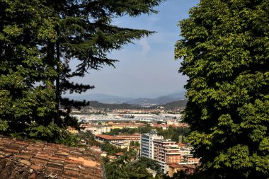 Gökyüzünden görünen şehir, güneşli bir günde ağaçlar ve çatılarla çevrili.