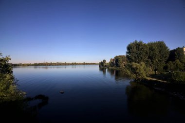 Göl kıyısında ağaçlar, gün batımında gökyüzünden görülüyor.