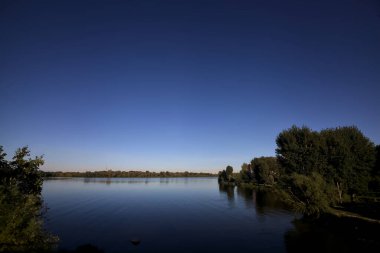 Göl kıyısında ağaçlar, gün batımında gökyüzünden görülüyor.