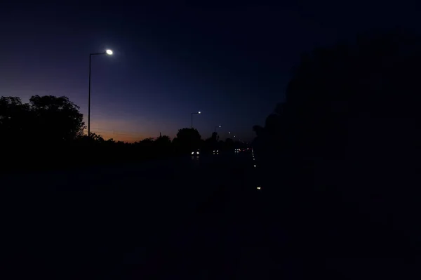 在一个公园旁边的路 黄昏的时候有车经过 — 图库照片